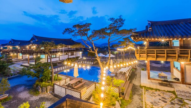 A traditional Japanese-style resort with multiple wooden buildings, a central pool, and string lights. - Gyeongju West Namsan Hanok Pension (Gyeongju)