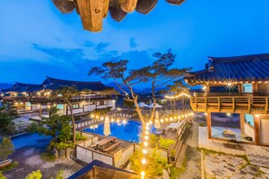 A traditional Japanese-style resort with multiple wooden buildings, a central pool, and string lights. - Gyeongju West Namsan Hanok Pension (Gyeongju)