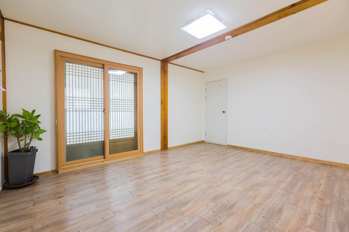 A room with wooden flooring, a sliding glass door, a potted plant, and a ceiling light fixture.