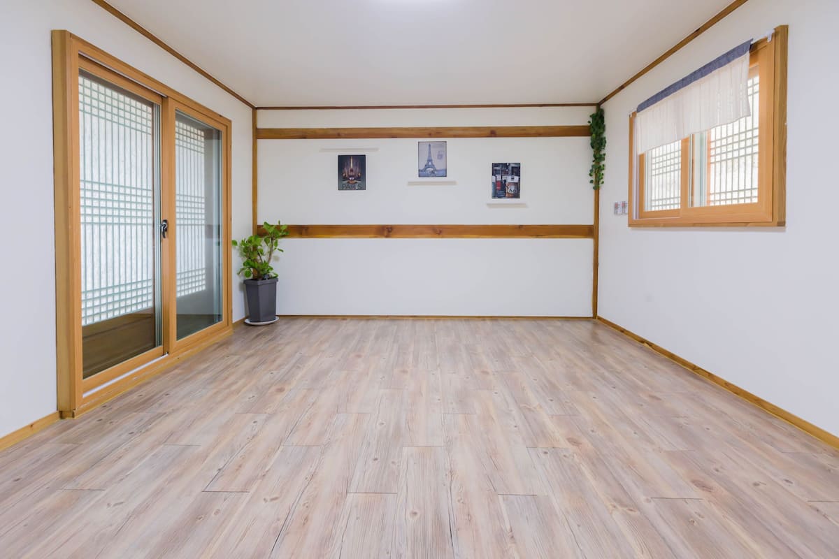 A room with wooden flooring, a sliding glass door, a potted plant, and three framed pictures on the wall.