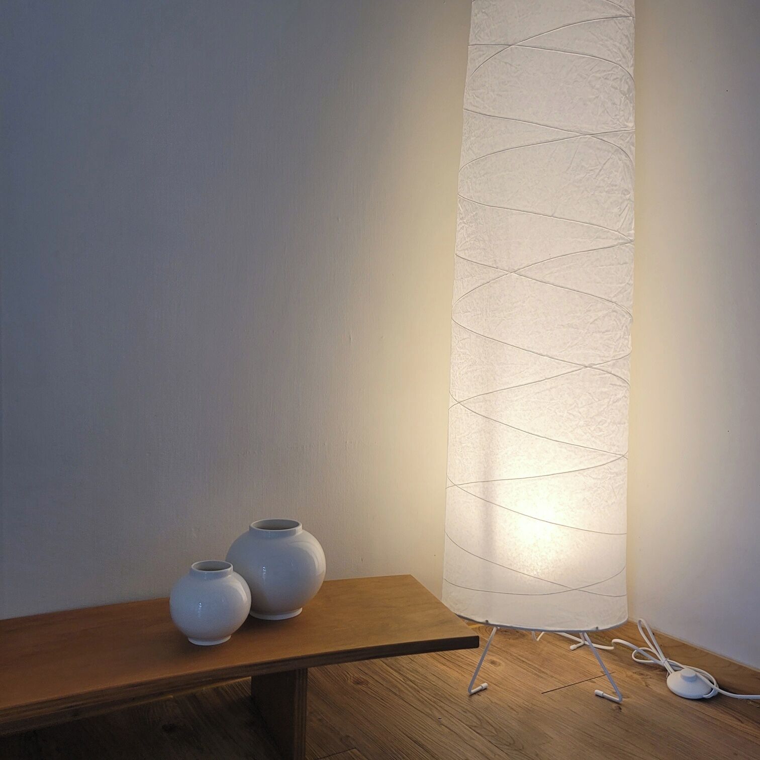 A wooden table with two white vases and a modern floor lamp with a textured lampshade.