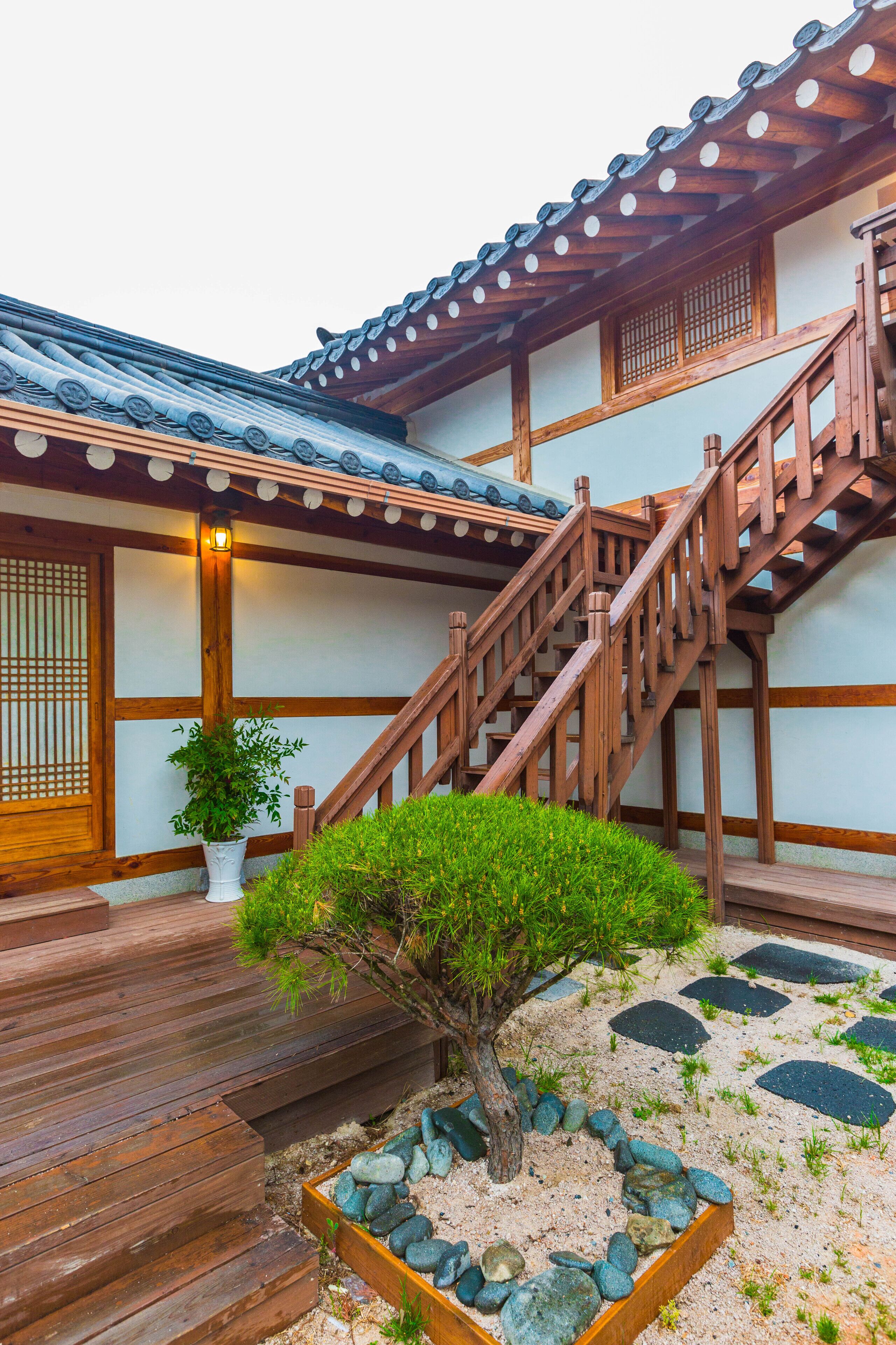 Un edificio de estilo japonés tradicional con una escalera de madera y un pequeño jardín rocoso con un árbol.