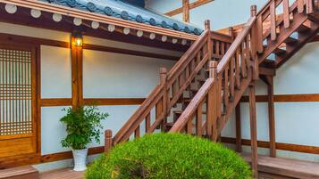 Un edificio de estilo japonés tradicional con una escalera de madera y un pequeño jardín rocoso con un árbol.