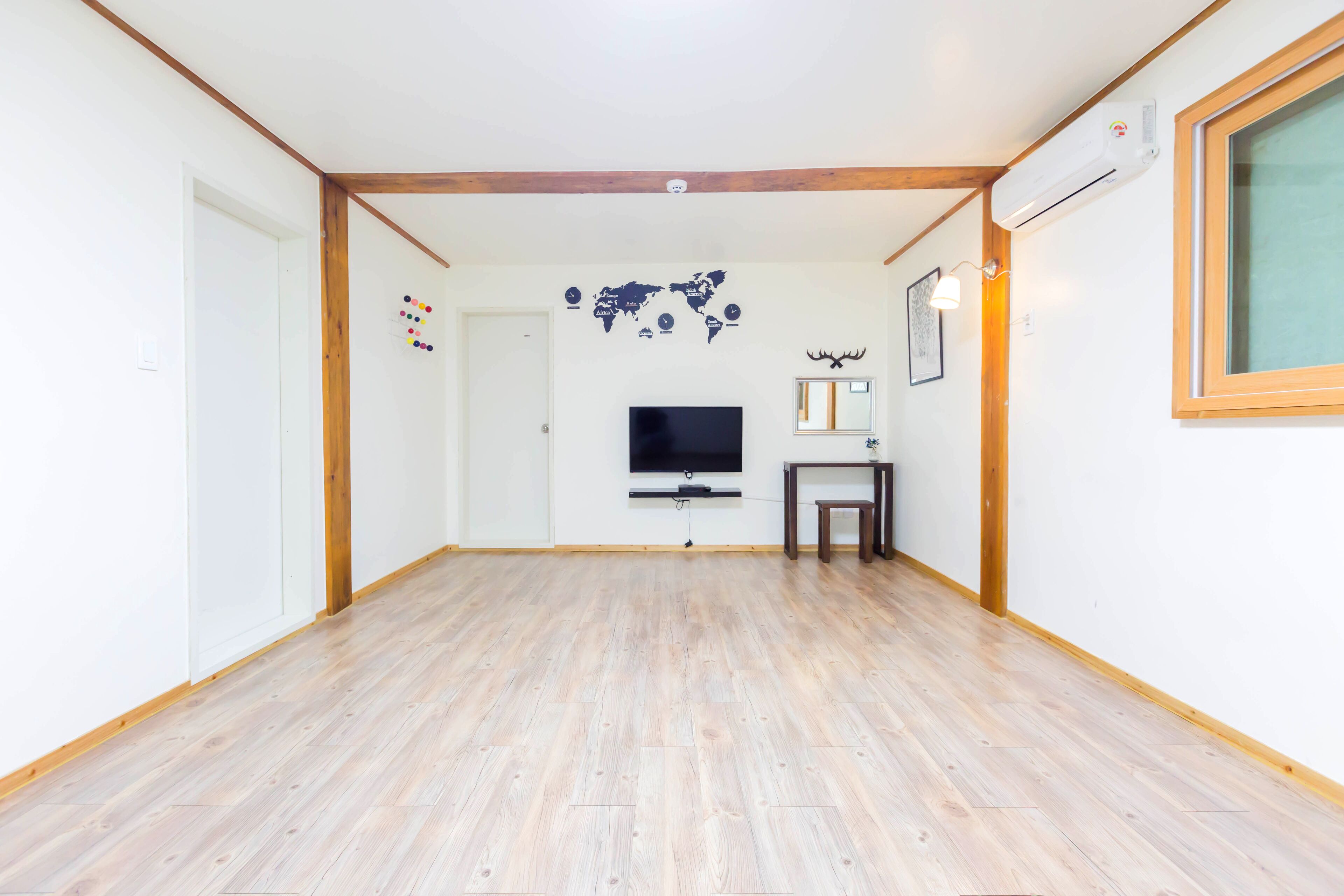 A spacious room with a wooden floor, a mounted TV, a small table, and a world map decoration.