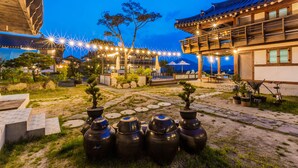 A traditional courtyard with stone pathways, potted plants, and a wooden building with a tiled roof. - Gyeongju West Namsan Hanok Pension (Gyeongju)