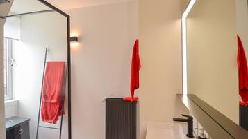 A bathroom with a glass shower enclosure, a white sink, a mirror, and a red towel hanging on the wall.