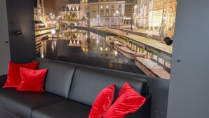 Habitació moderna amb un sofà de cuir negre, coixins vermells i un mural gran amb una escena d'un canal.