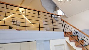 A multi-level interior with a wooden staircase, a chandelier, and a grid-patterned railing. - Gyeongju Olive House Pension (Gyeongju)