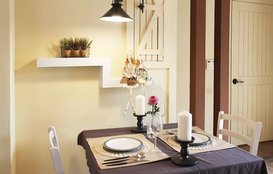 Una mesa de comedor dispuesta con platos, cubiertos y velas, con una silla blanca y un colgante sobre ella.