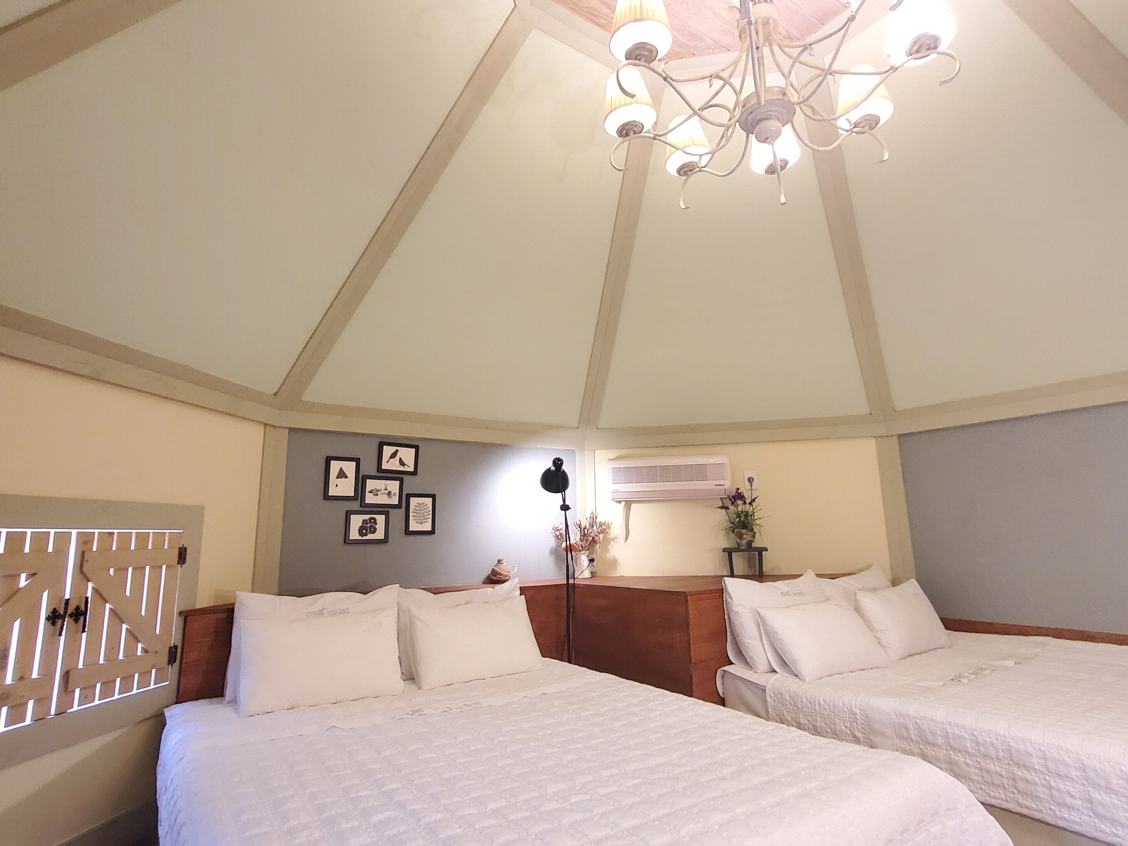 A hotel room with two beds, a chandelier, wall-mounted air conditioning, and framed pictures.