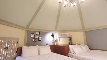A hotel room with two beds, a chandelier, wall-mounted air conditioning, and framed pictures.