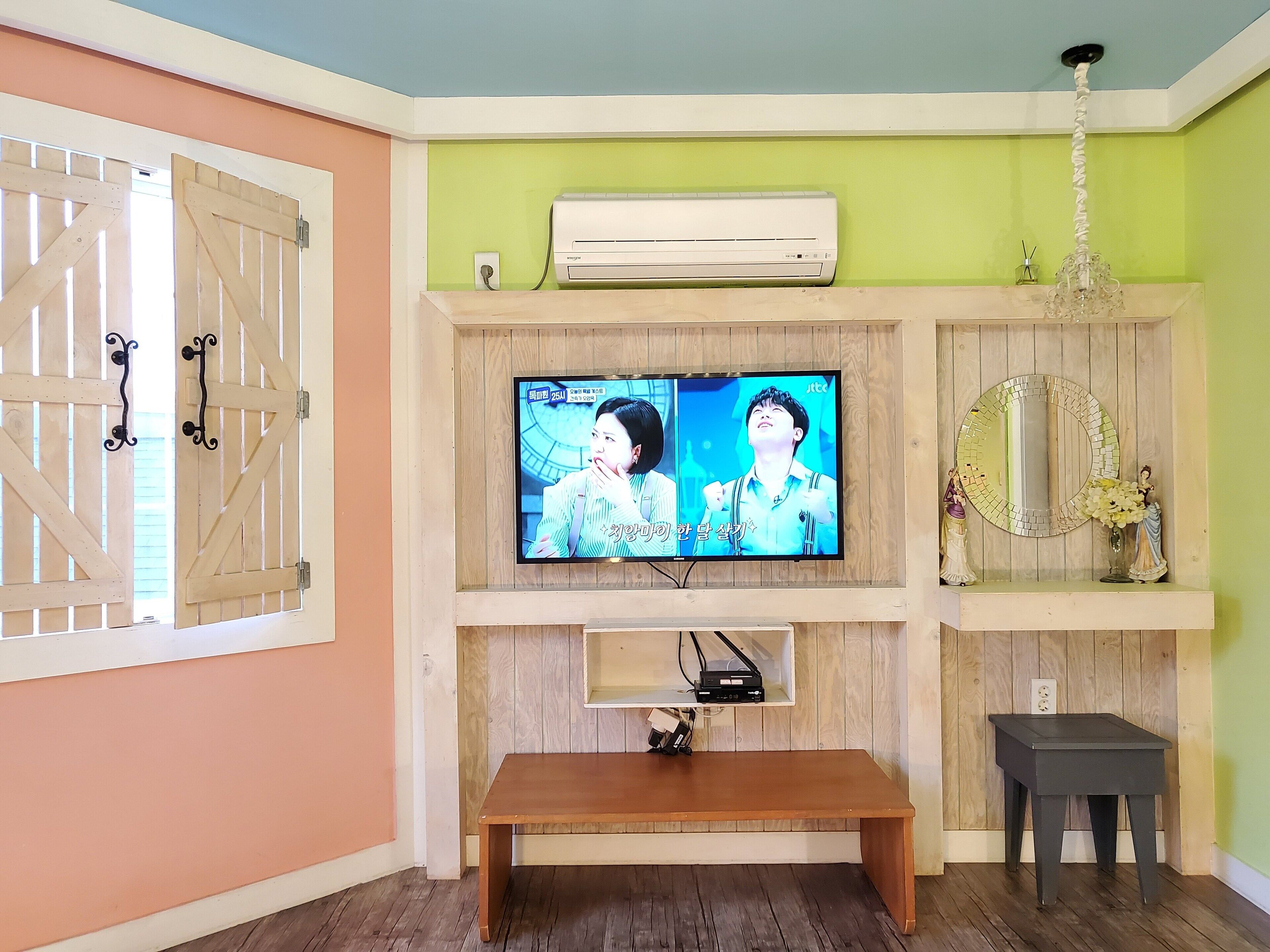 A living room with a TV mounted on a wooden wall, a bench, a small table, and a decorative mirror.