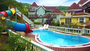 A swimming pool with a slide, surrounded by colorful houses with distinct architectural styles. - Gyeongju Olive House Pension (Gyeongju)