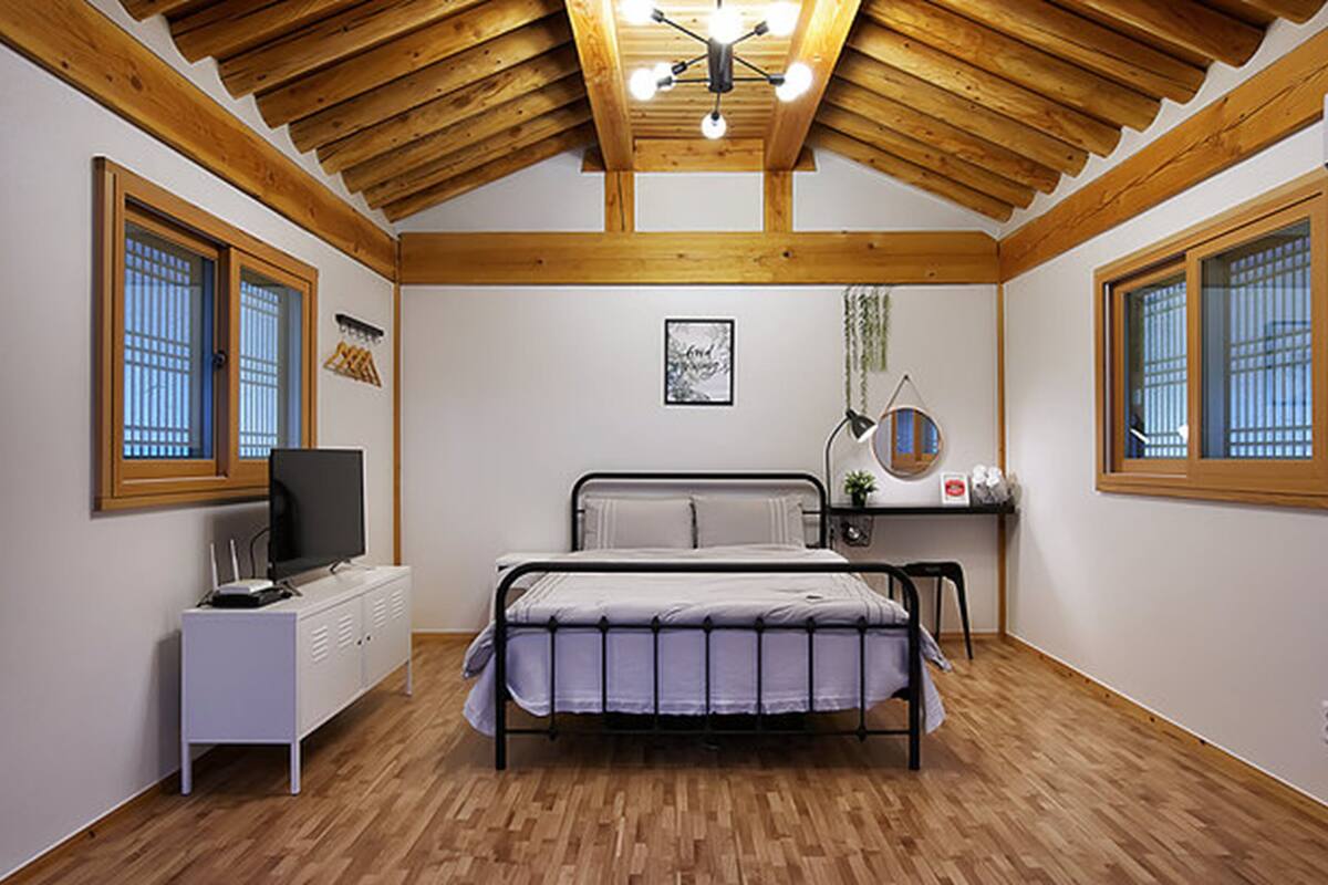 Ein Schlafzimmer mit Bett, Schreibtisch, Stuhl, Fernseher und Fenster.