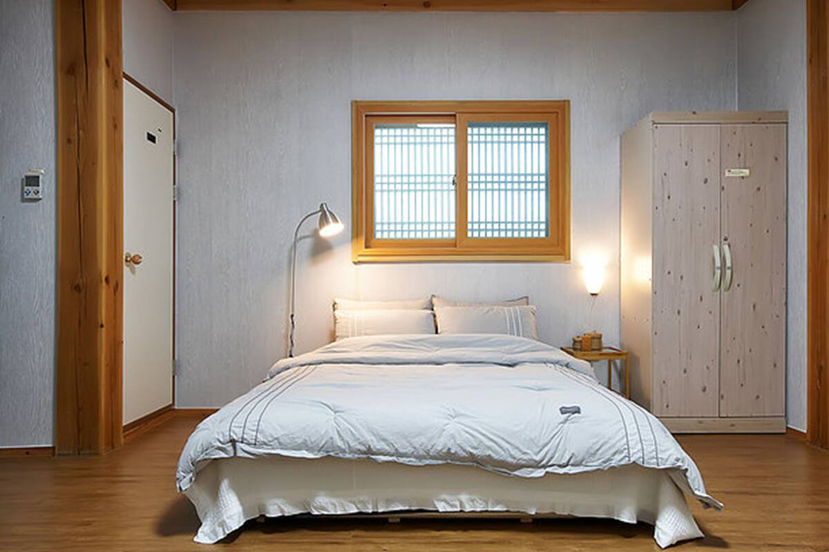 Ein Schlafzimmer mit Bett, Nachttisch, Kleiderschrank und einem Fenster mit Jalousien.