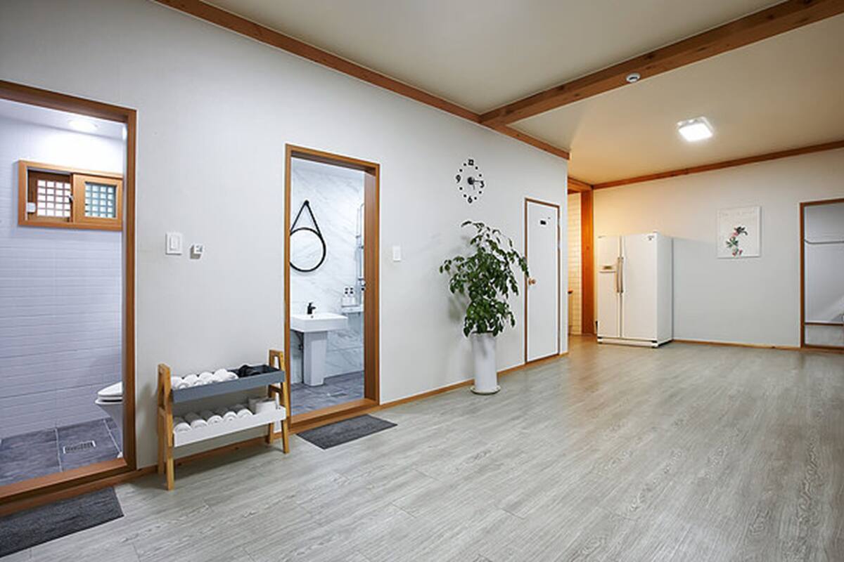 Ein geräumiges Zimmer mit Holzboden, einer weißen Tür, einem weißen Kühlschrank und einem Blumentopf.