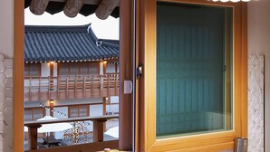 Una habitación japonesa tradicional con suelo de tatami, puertas correderas de shoji y vistas a un edificio de madera con tejado de tejas.