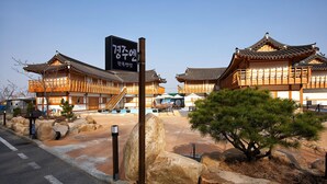 Un edificio tradicional coreano con un letrero, rocas grandes y un pino al frente.