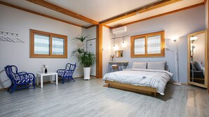 Un dormitorio con cama, dos sillas, una mesita, una planta en maceta y un espejo.