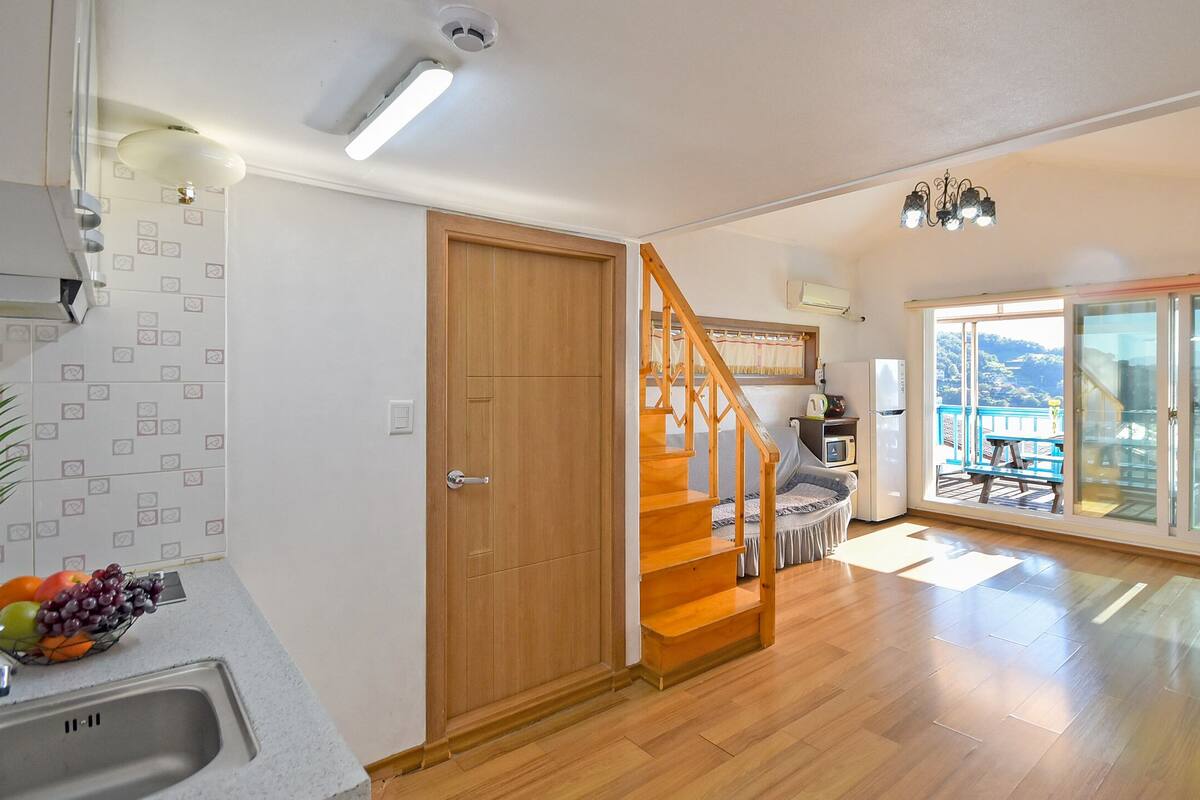 Ein geräumiger Wohnbereich mit einer Holztreppe, einer Küche mit Obstschale und einem Balkon mit Blick.