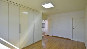 A room with a wooden floor, white walls, and a ceiling light. There is a door on the right and a wardrobe on the left.