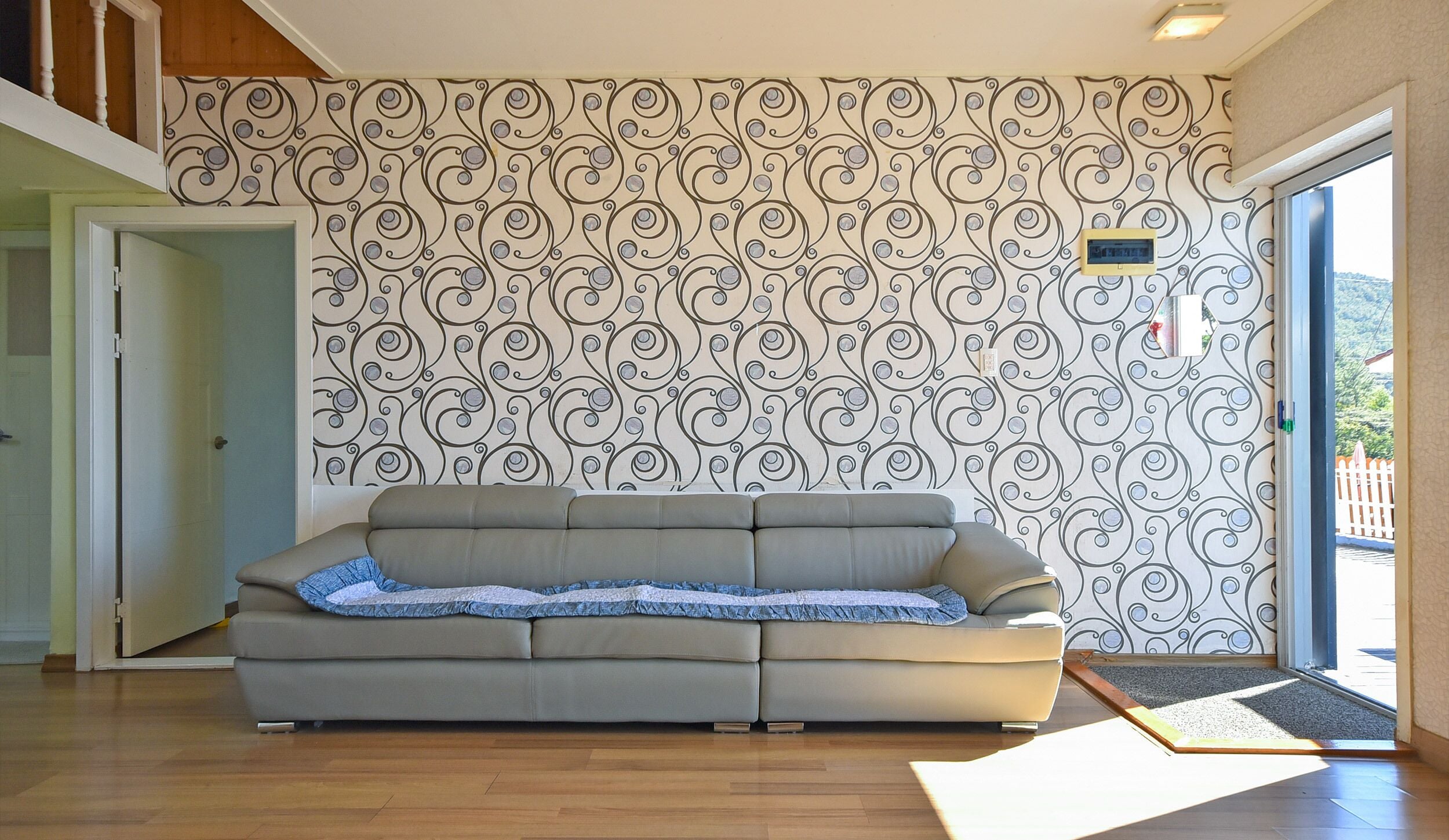 Un soggiorno con carta da parati decorata, un divano grigio e un pavimento in legno.