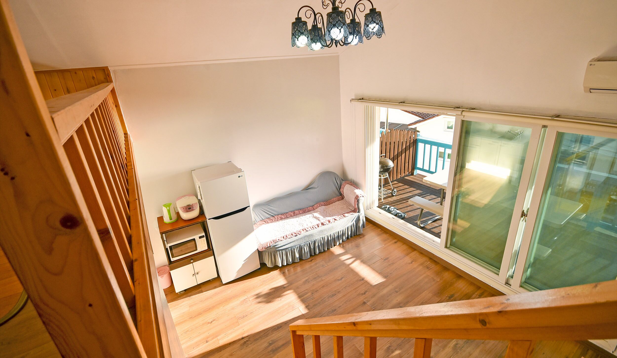 A small, compact room with a bed, a microwave, a refrigerator, and a wooden staircase.
