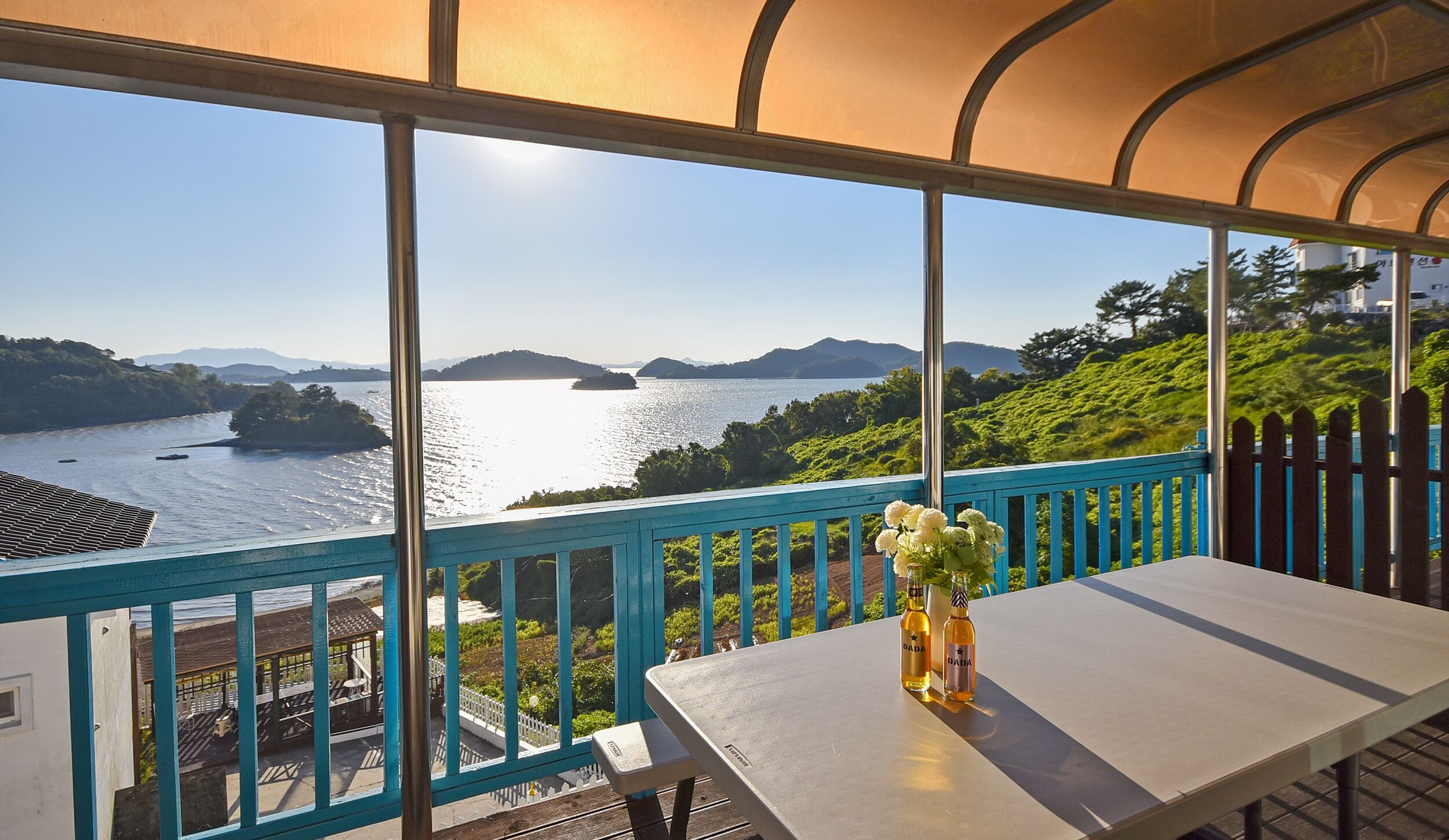Un balcon avec une table, un vase rempli de fleurs et une vue sur un lac et des montagnes.