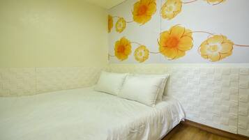 Un dormitorio con cama, ropa de cama blanca, un mural floral en la pared y un cabecero blanco texturizado.