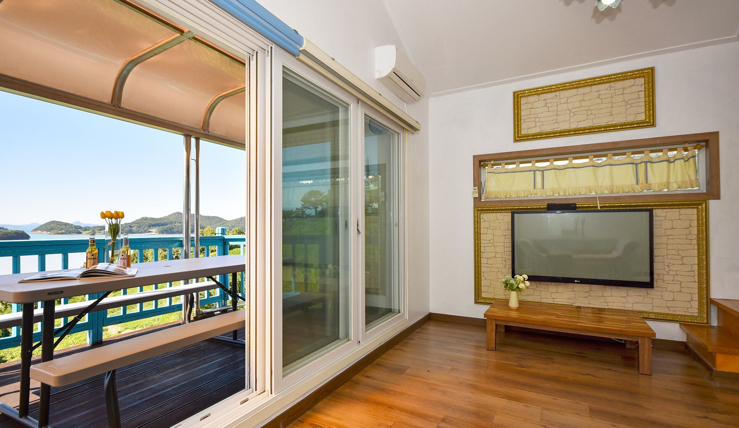 Een balkon met een houten tafel, een bank en uitzicht op zee.