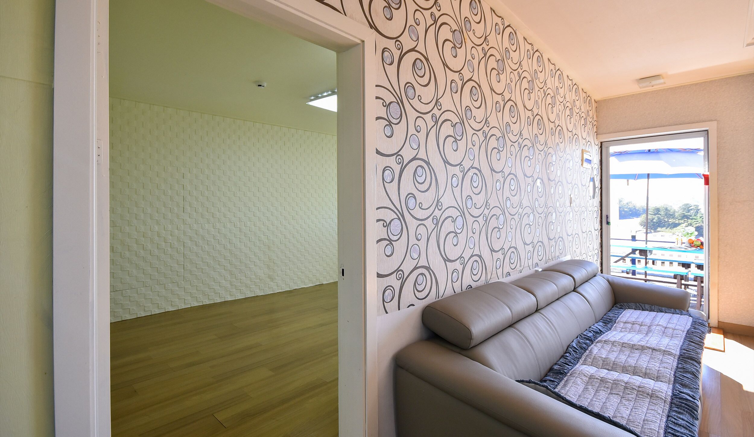 Una habitación con pared estampada, suelo de madera y sofá color beige con colcha.
