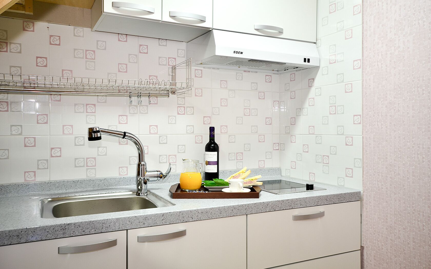 A kitchen with a stainless steel sink, a wine bottle, and a tray with food items.
