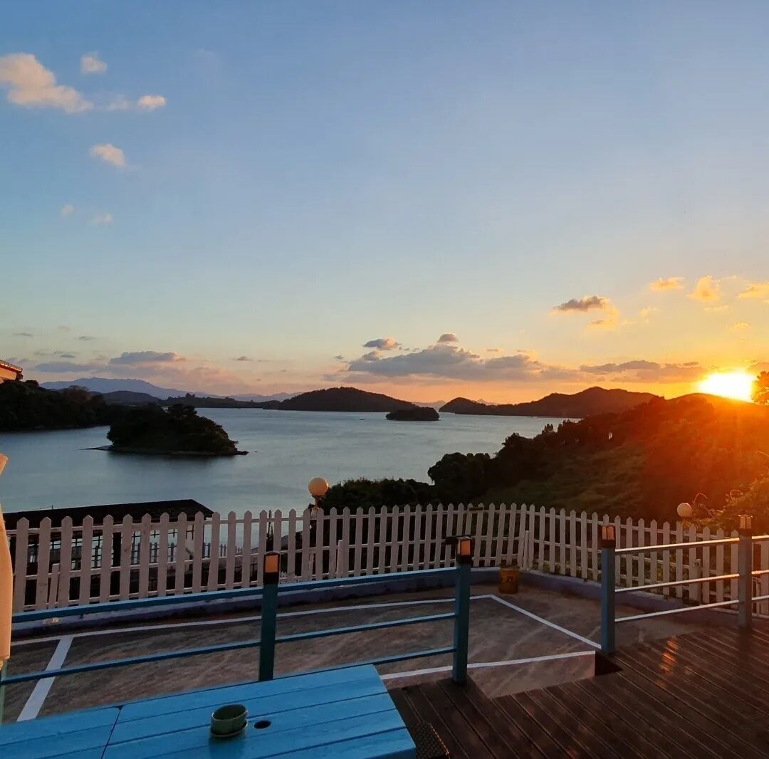 Une terrasse offrant une vue sur un coucher de soleil au-dessus de l’eau et des collines.