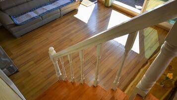Een houten trap met een witte balustrade leidt naar een kamer met een grijze bank en een houten vloer.