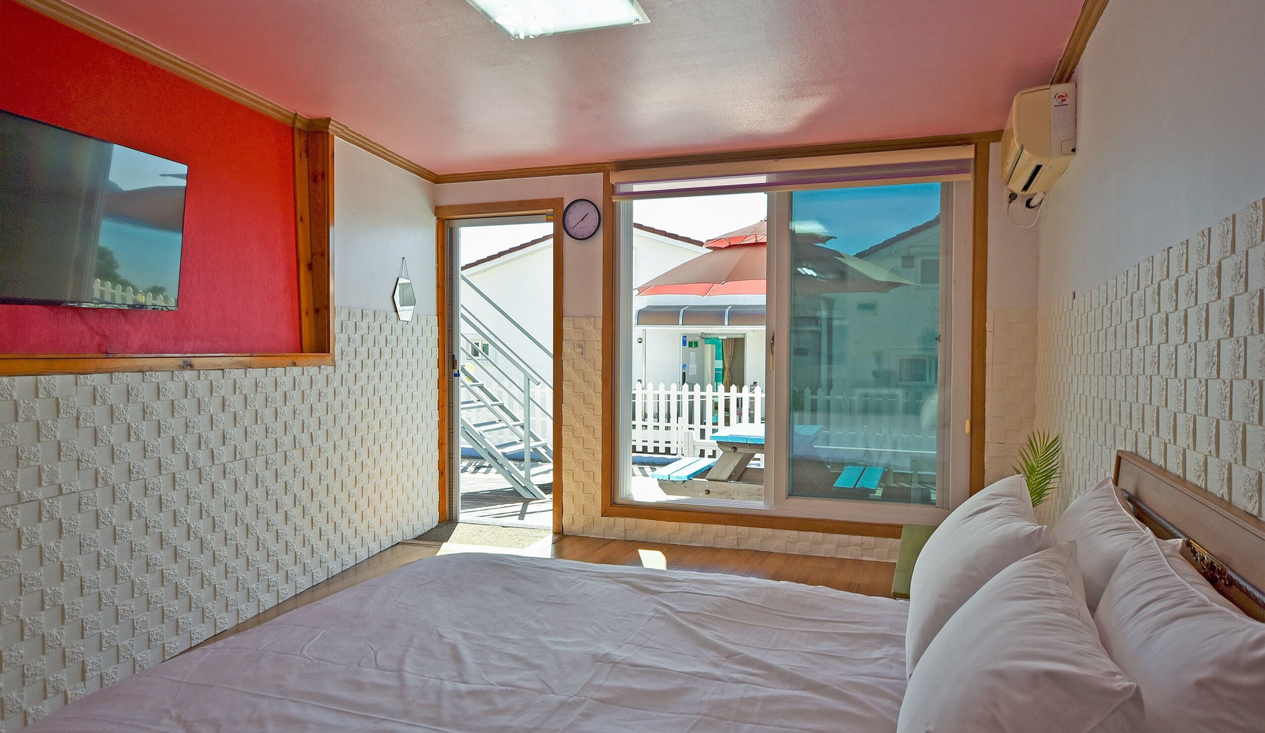 A bedroom with a bed, a window with a view of a balcony, and a clock on the wall.
