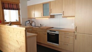 A modern kitchen with wooden cabinets, a built-in oven, and a window with a striped valance. - Appartement Moilles 15 (Val d'Illiez)