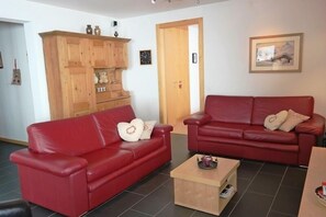 A living room with two red leather sofas, a wooden cabinet, and a small wooden coffee table.