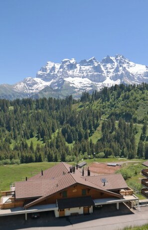A mountain lodge with a sloped roof, a parking area, and a view of snow-capped mountains.