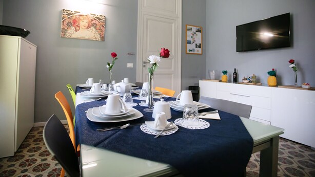 A dining area with a table set for four, a white cabinet, a television mounted on the wall, and a door with a white frame. - Belle Epoque B&B (Trapani)
