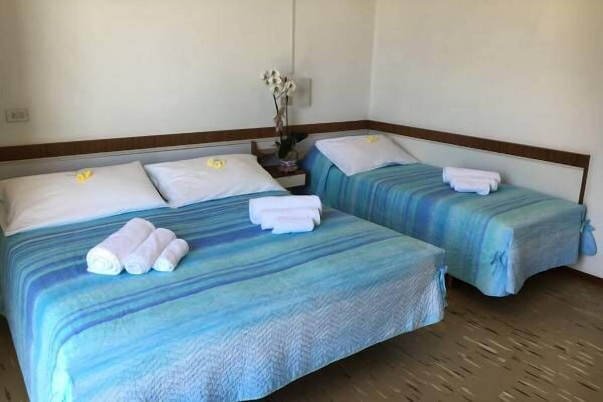 Een hotelkamer met twee bedden, elk met een blauw gestreepte spreidek en witte kussens. Er liggen handdoeken netjes gevouwen op elk bed.