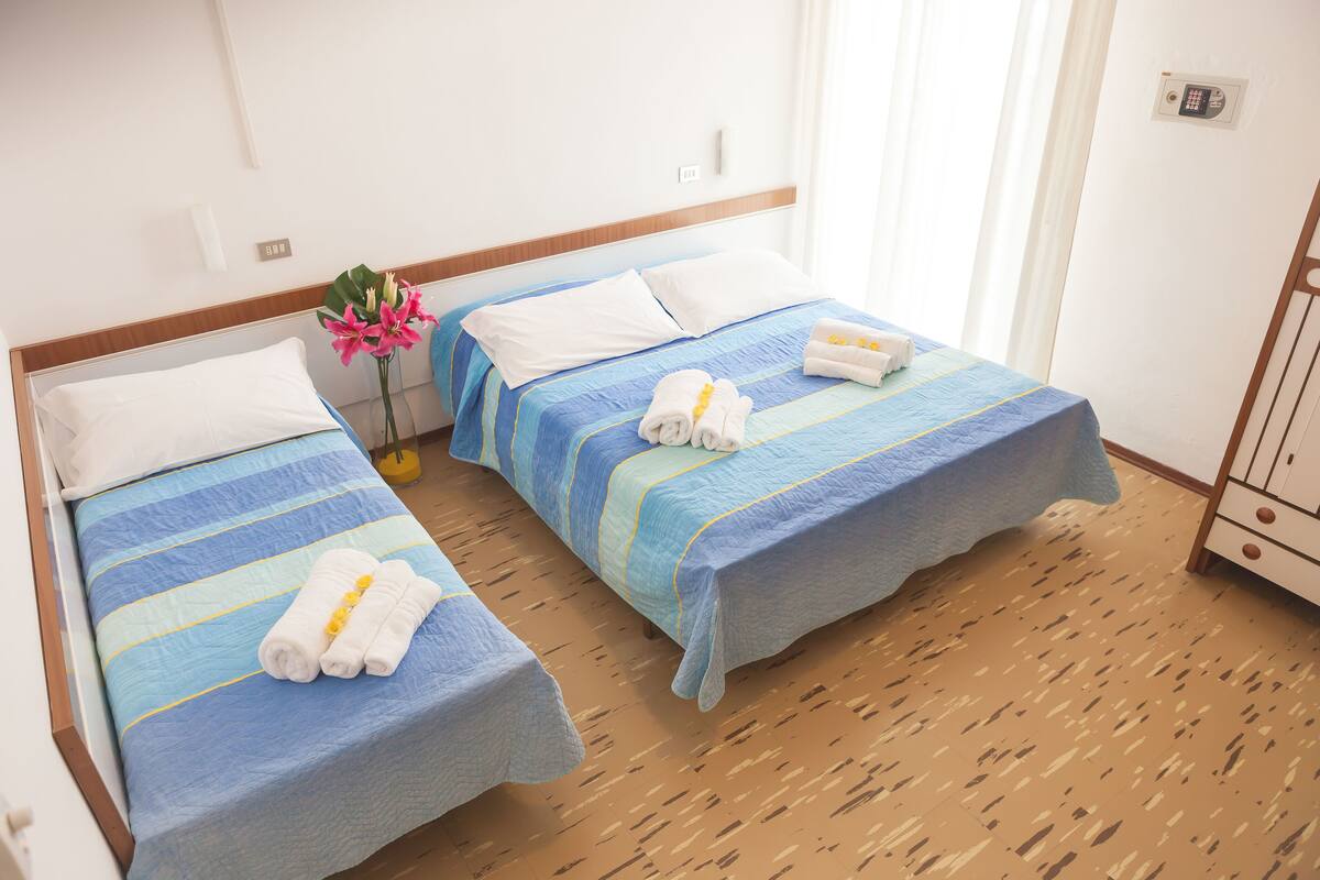 Een hotelkamer met twee bedden, elk voorzien van een blauw gestreept dekbedovertrek en witte kussens. Op de bedden liggen handdoeken en op het nachtkastje staat een vaas met bloemen.