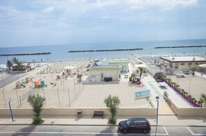 A beachside hotel with a parking lot, beach umbrellas, and a view of the sea.