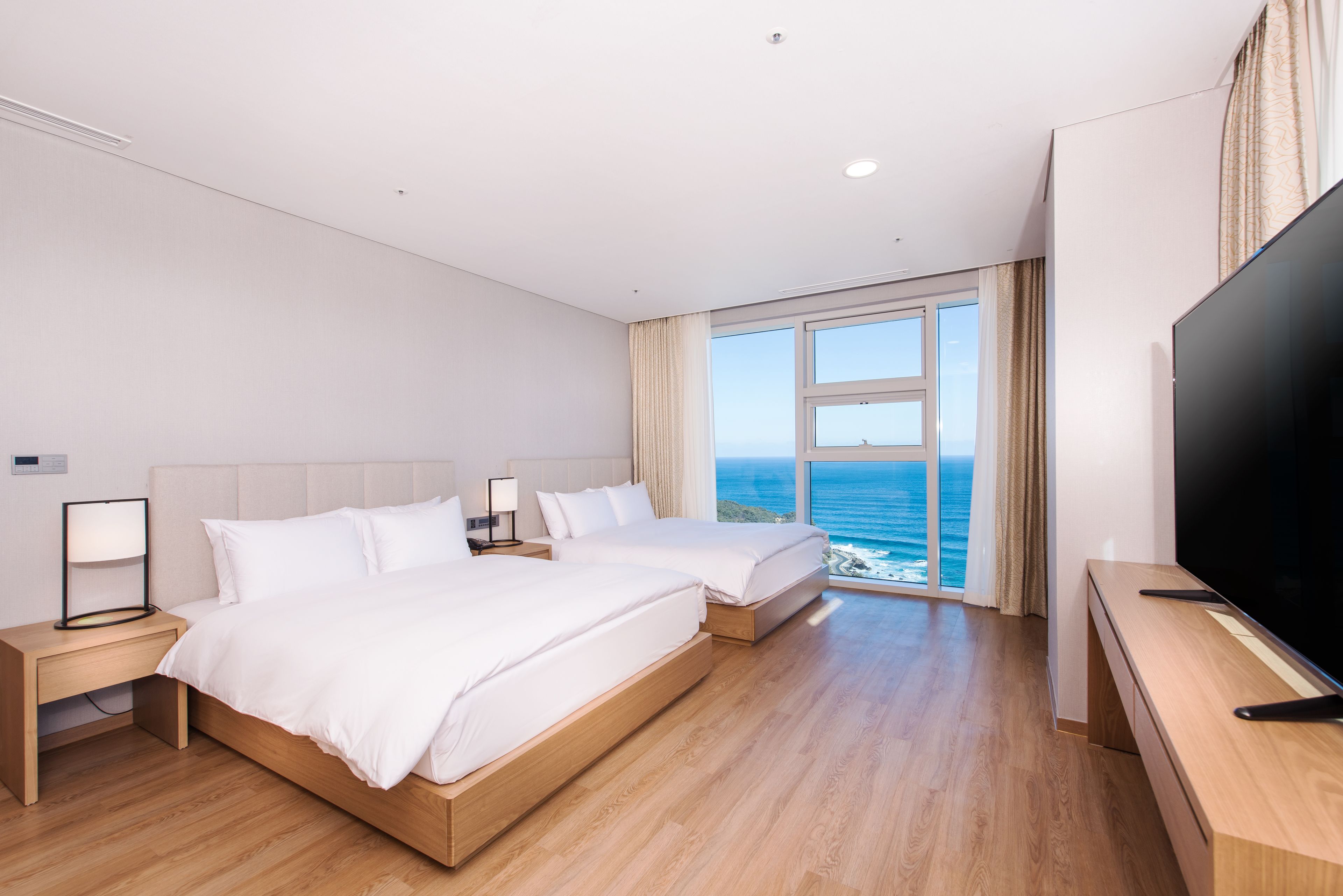 A hotel room with two beds, a TV, and a large window with a view of the ocean.