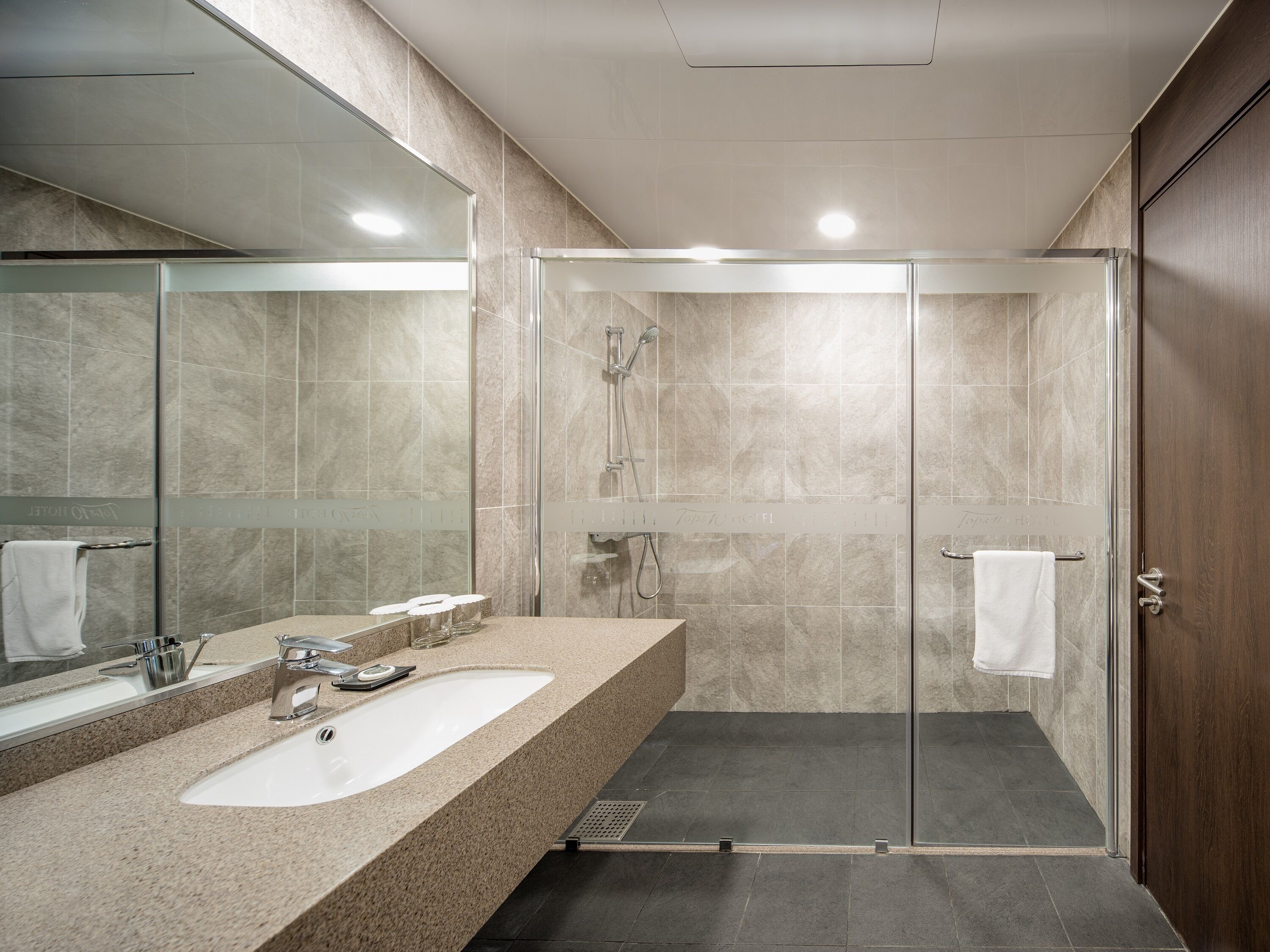 A modern bathroom with a large mirror, a sink, and a shower area.