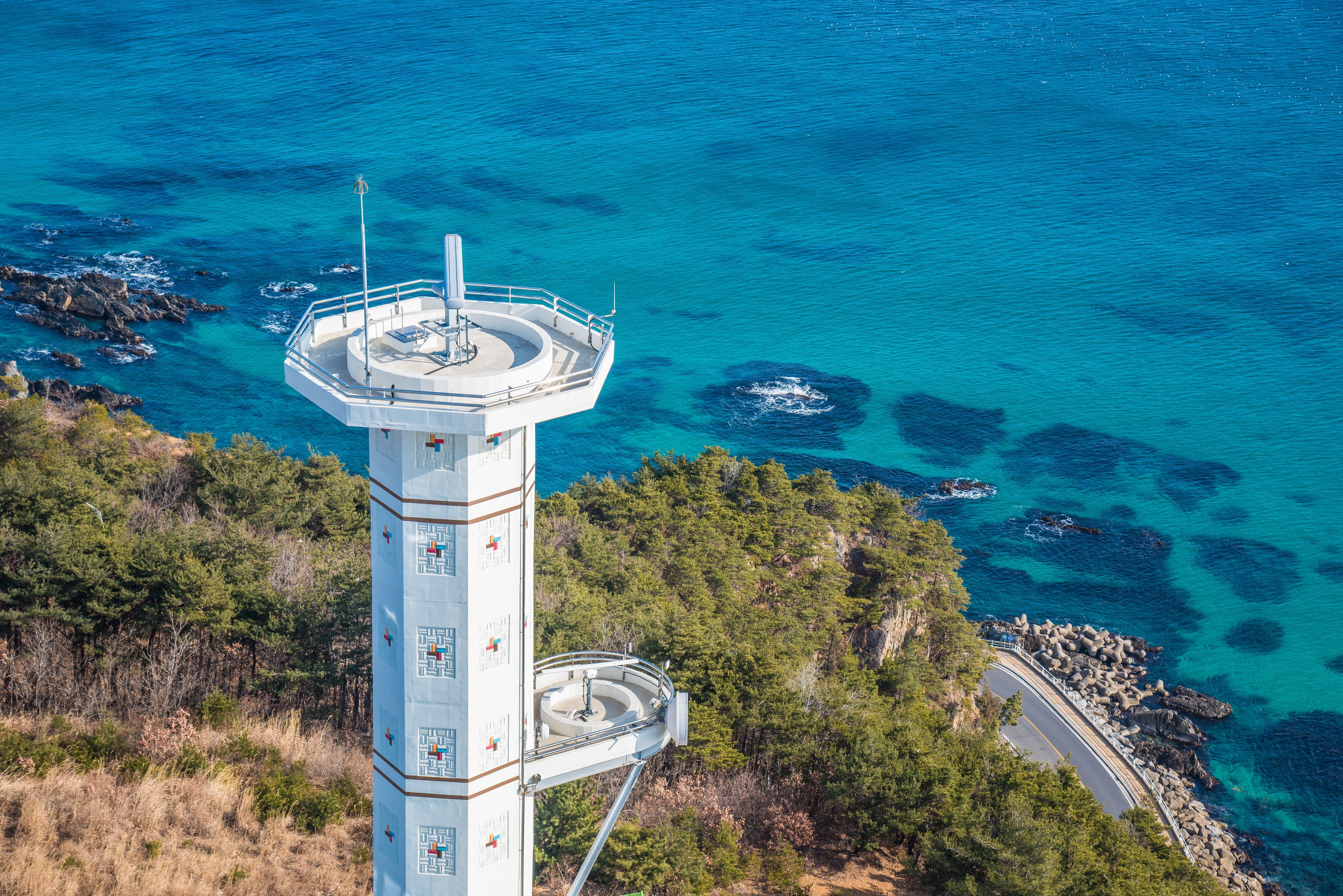 A lighthouse with a circular viewing platform, surrounded by rocky coastline and clear blue waters.