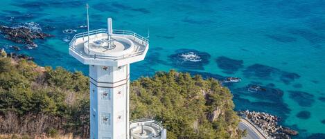 A lighthouse with a circular viewing platform, surrounded by rocky coastline and clear blue waters.