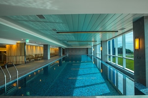 Una piscina con suelo de baldosas, zona de descanso y vistas al exterior a través de amplias ventanas.