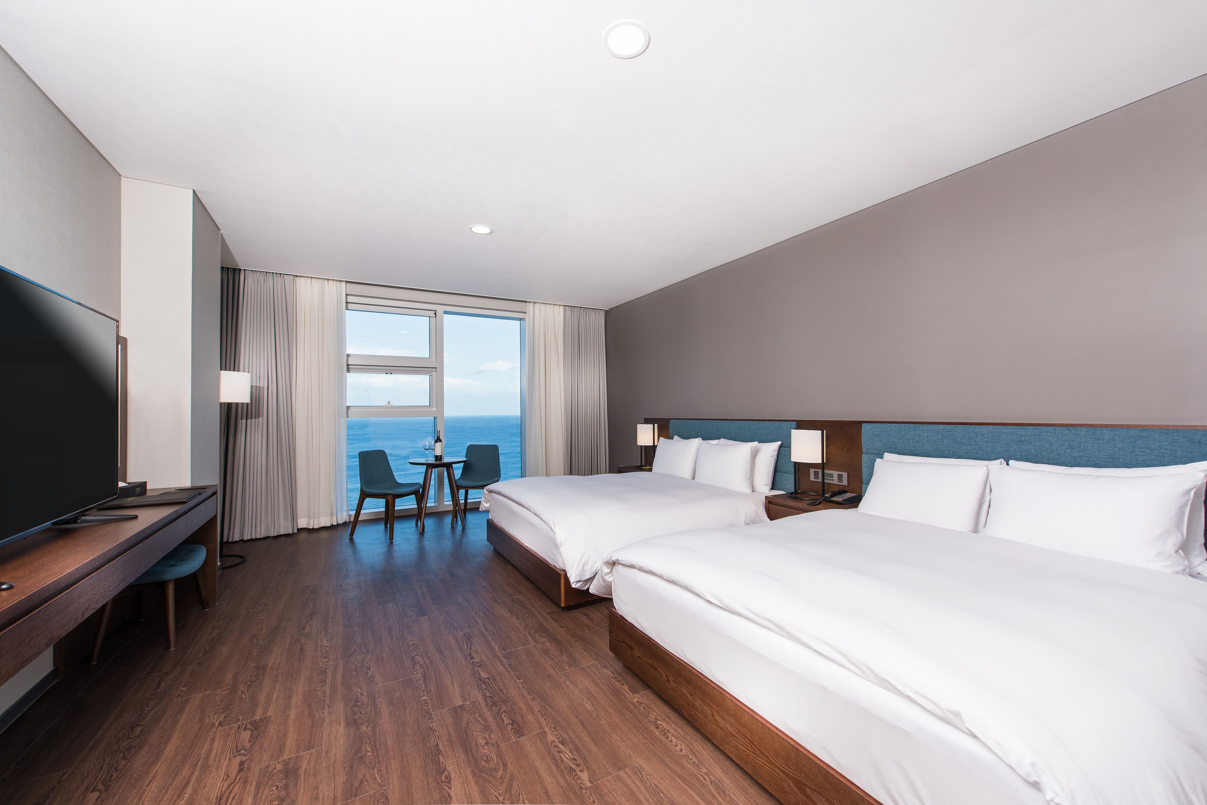 Een hotelkamer met twee bedden, een bureau, een televisie en uitzicht op zee.