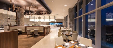 Un restaurante moderno con una barra larga, techo alto y ventanas amplias.