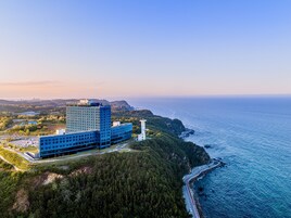 Un hotel moderno con fachada de vidrio, situado en un acantilado costero con vistas al mar.
